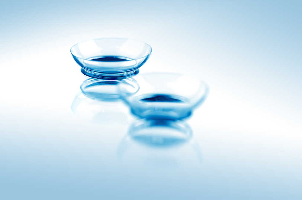 Two contact lenses with reflections on blue surfaces. Focus on long-distance lens. ** Note: Shallow depth of field